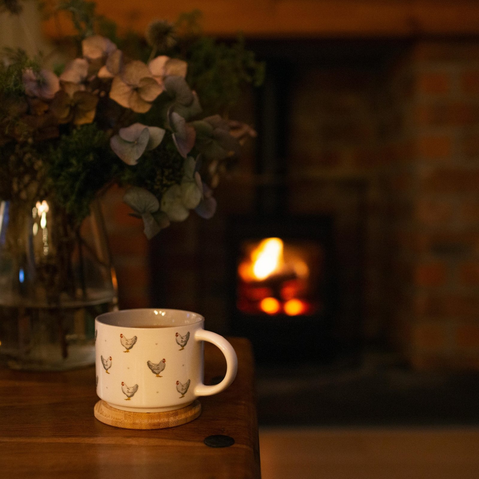 Charming mug with chicken design on a wooden table by the fireplace, surrounded by dried flowers for a cozy ambiance.
