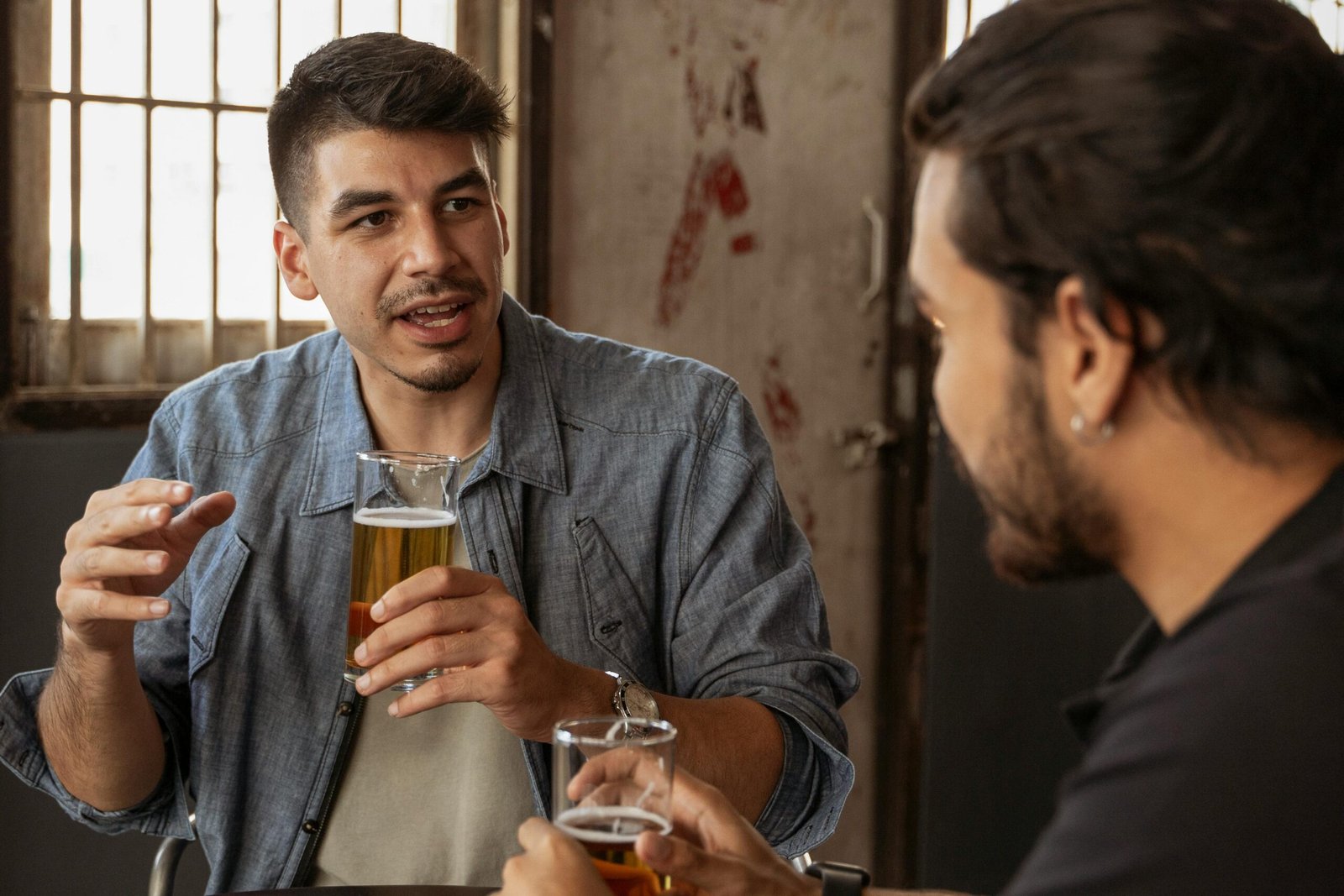 Two men enjoying a casual conversation with beers in an indoor café setting.