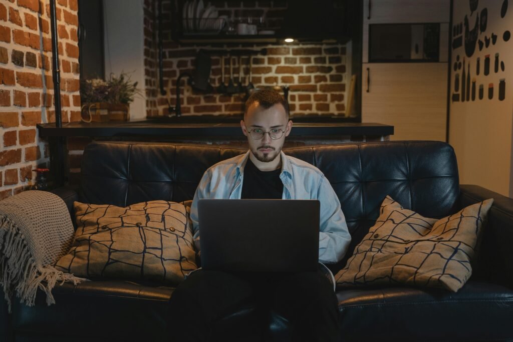 Man working remotely on a laptop in a cozy, stylish apartment with exposed brick walls and modern decor.
